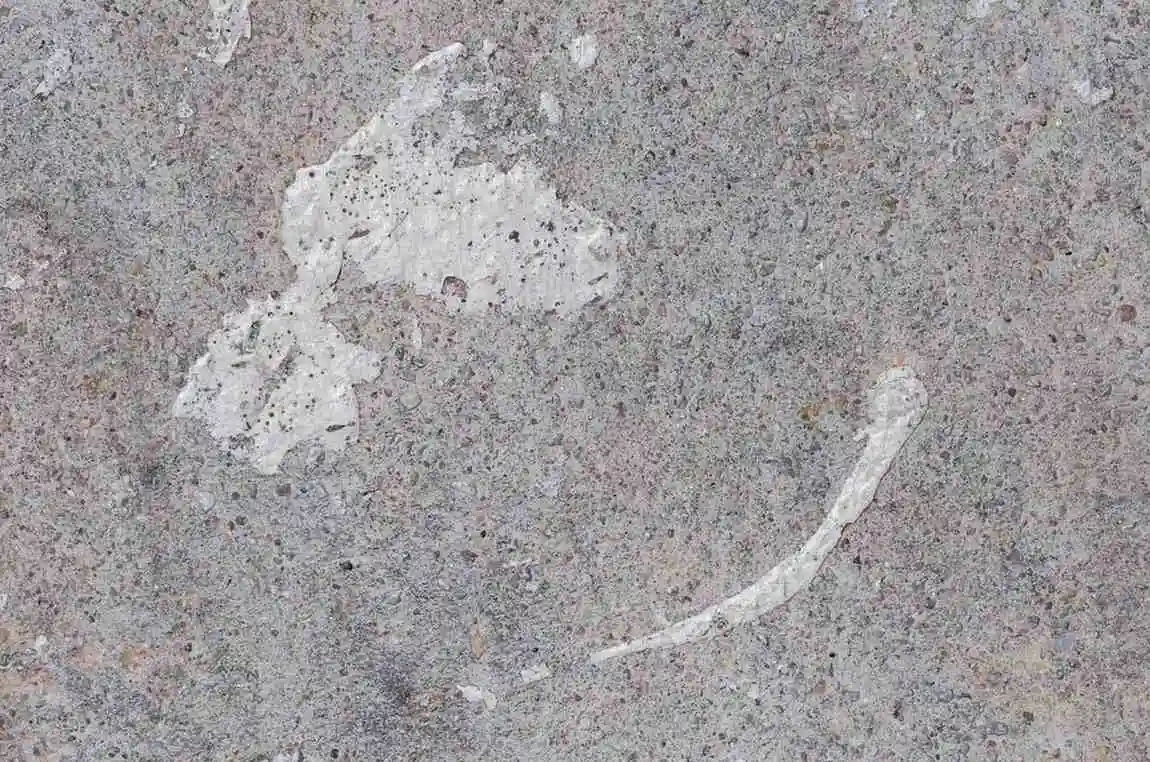 A close-up view of a grey marble surface showing white, chalky etched patches and pitted corrosion caused by acidic damage.