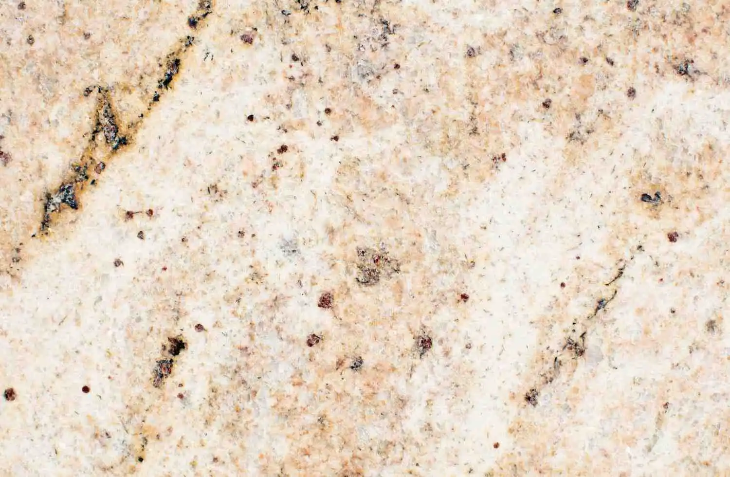 A close-up view of a polished cream and beige granite surface featuring intricate speckles of brown, black, and gold minerals that create a busy natural pattern.