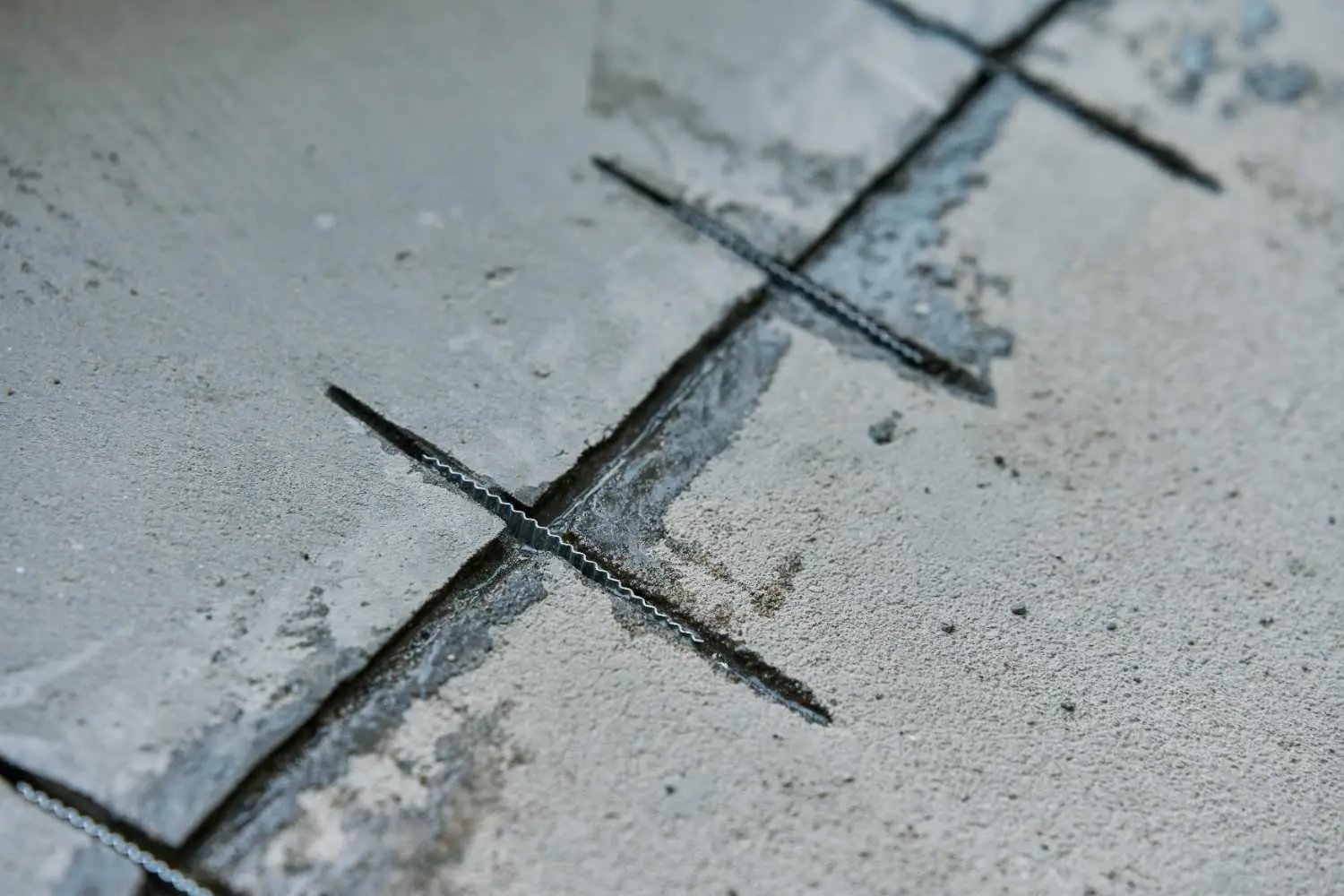 Close-up of metal staples embedded in a concrete floor to repair and stabilize a structural crack using stitching.