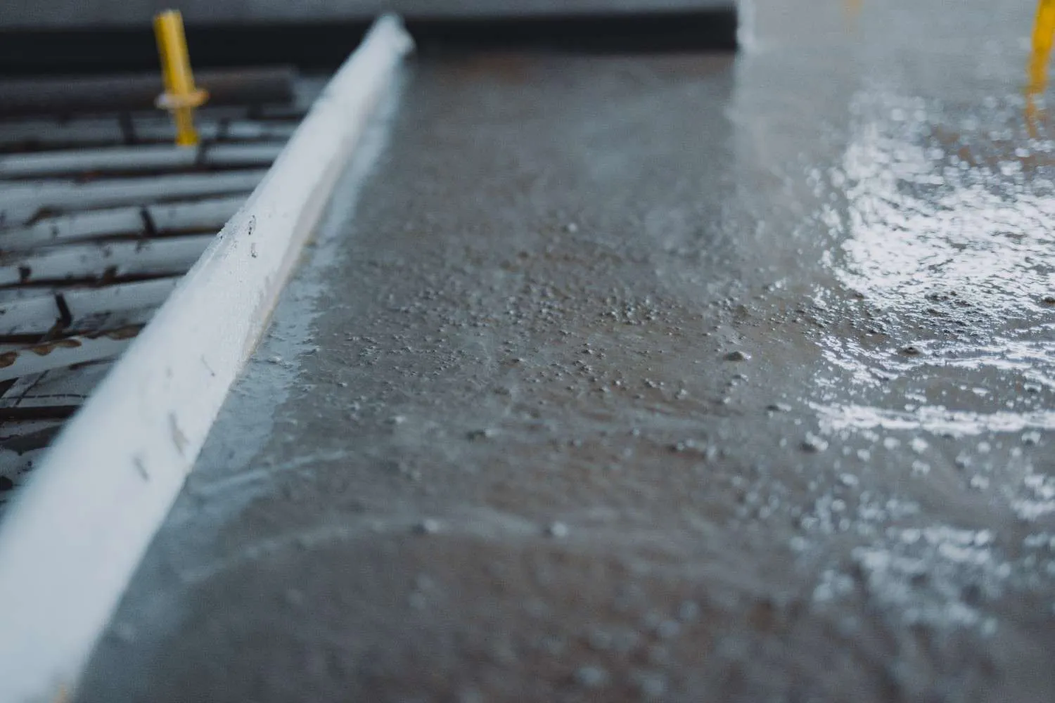 A close-up view of fresh wet concrete or self-leveling overlay being smoothed over a damaged floor with metal reinforcement visible in the background.